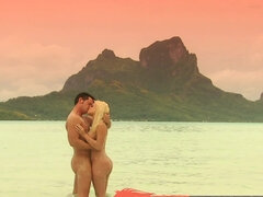 A blonde is by the ocean with her lover and she is kissing him there